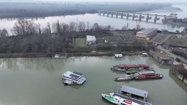Isola Serafini hydroelectric dam and navigation bridge across the Po River near Monticelli d'Ongina, Piacenza Province, Emilia-Romagna, Italy with barges and industrial river port area