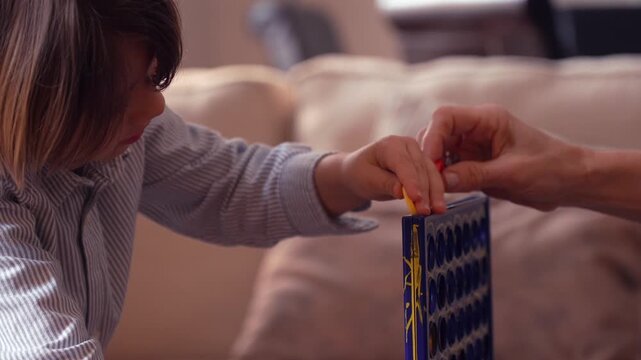 Mother and son playing a four in a row board game together developing logic and strategic thinking at home in the living room