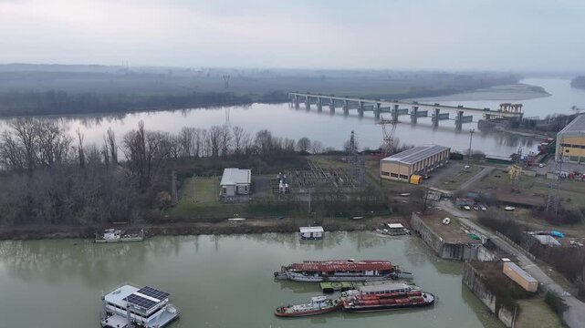Isola Serafini Dam spanning the Po River near Monticelli d'Ongina, Piacenza Province, Emilia-Romagna, Italy with navigation bridge and river barges in floodplain landscape