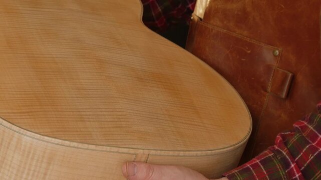 Luthier demonstrates tight wood grain in body of acoustic guitar, CU