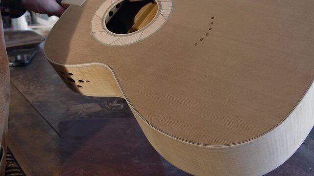 Luthier shows acoustic guitar body in development on workbench, closeup