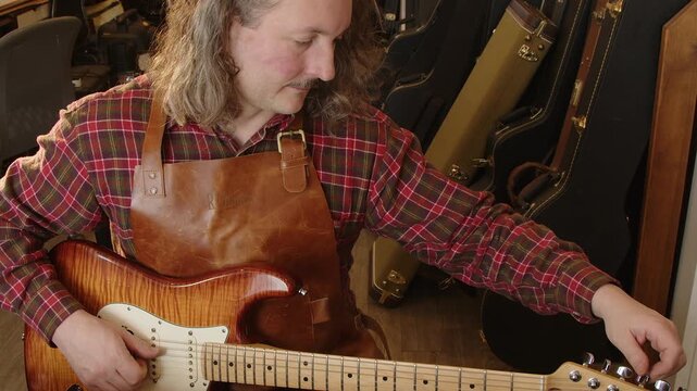 Guitar technician sitting at work bench tunes maple electric guitar