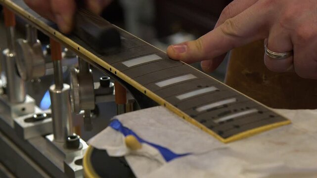 Guitar tech in repair shop fills and sands ebony fretboard in refret