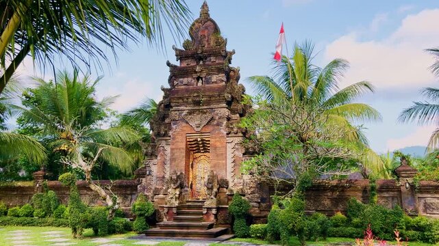 Decorative stone temple gate in Bali featuring classic Balinese Hindu architecture surrounded by lush tropical garden plants and tall palm trees in a peaceful cultural setting.