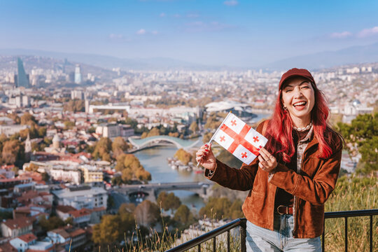 Cheerful woman holding a Georgia flag enjoying the panoramic view of Tbilisi cityscape and the Kura River