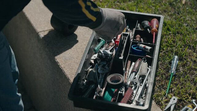 Open toolbox filled with assorted hand tools placed on ground outdoors