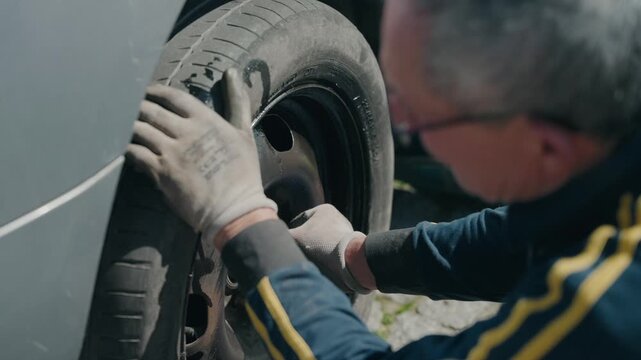 lifting and positioning car tire onto wheel hub while vehicle is raised with jack on paved driveway