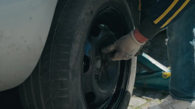 mounting car tire onto vehicle hub during tire change on paved driveway