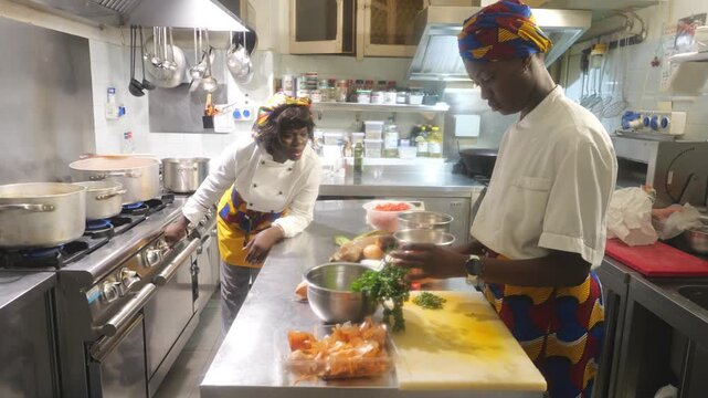 A skilled female chef in a vibrant headwrap and chef's coat meticulously chops herbs and tends to simmering pots on a professional gas range