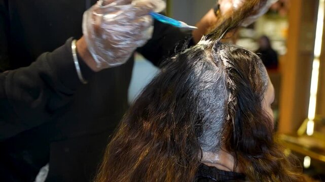 Hairdresser applying dye to a client&rsquo;s hair roots using a brush while wearing protective gloves
