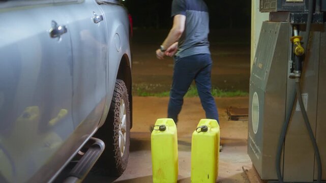 4x4 vehicle at a service station at night, desperate man unloads fuel jerry containers from vehicle and places them beside the fuel bowser. Clip 10