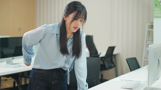 Young office worker experiencing lower back pain backache expression, symptom painful spinal ache, hand holding massaging or rubbing after long time study working on computer, incorrect posture