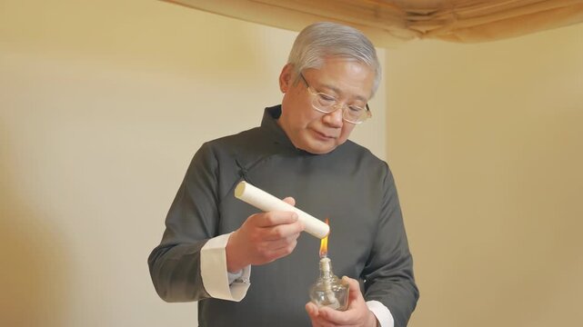 Traditional therapist treatment, practitioner acupuncturist senior man lighting up moxa sticks, performing moxibustion procedure, burning moxa herb roll with smoke. Concept of alternative medicine.