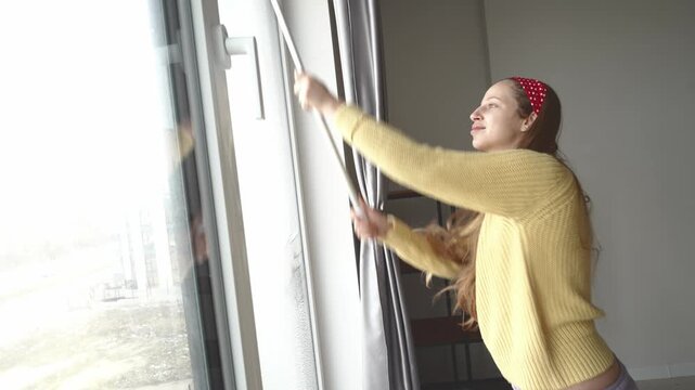 Pregnant woman wiping a window at home as part of spring cleaning. Household maintenance, tidy interior, domestic lifestyle, hygiene and home care routine, practical indoor chores.