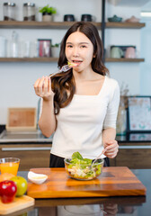 Asian young pretty positive woman standing in kitchen prepare making eating healthy salad from...