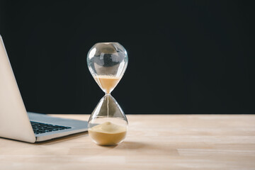 Hourglass, time glass, hour, sand clock, timer visualize business growth concept, urgency for deadline countdown, laptop rests on wooden desk to optimize business progress