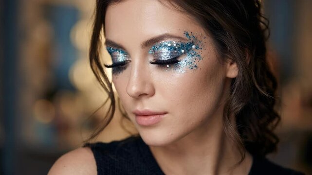 Close-up of a young woman's face with artistic blue glitter eye makeup and false eyelashes