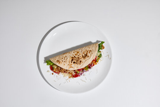 Tortilla wrap filled with vegetables, meat and cheese served on white plate on clean white background top view. Concept of street food, takeaway meal, casual dining and food delivery menu design.