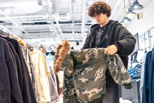 Teenage Boy Choosing Camouflage Jacket in Clothing Store, Youth Fashion Shopping and Retail Concept
