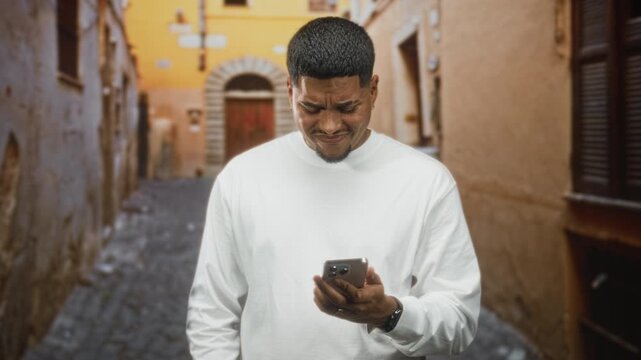 Man holding smartphone and frowning while checking messages with both hands on device in a narrow street; frustration.
