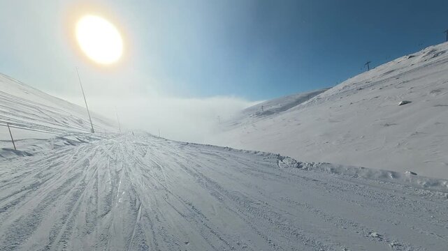 POV snowboarding down a slope through fog under bright sun and clouds. Action camera footage capturing speed, changing visibility, and atmospheric winter mountain conditions.