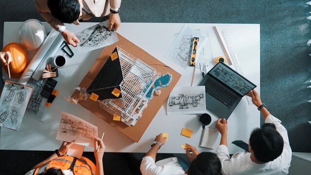 Top view of manager handed blueprint to professional engineer team at meeting table with house model and project plan. Group of architect discussing about design while receive document. Alimentation.