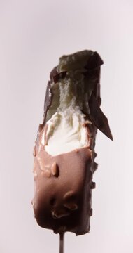 Closeup Video of bitten off Chocolate Almonds Ice Cream Stick Bar Rotating on White Background. Vertical Studio Shot, Local Light, 60 fps.