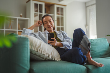 Fototapeta premium Asian woman relaxing on couch using smart phone