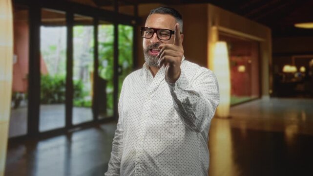Man with beard and glasses reaching hand forward and blowing a kiss in building; playful invitation.