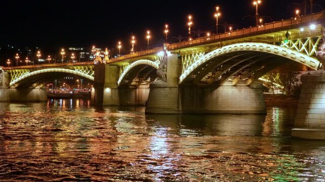 Stunning night view of the illuminated Margaret Bridge in Budapest, Hungary. The golden lights reflect beautifully on the Danube River surface, showcasing European architecture and city travel