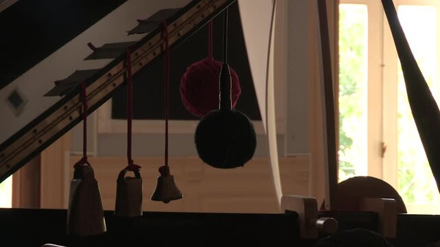 The lid of an open black piano, with rattles hanging from it and a microphone inside a ball of wire.
