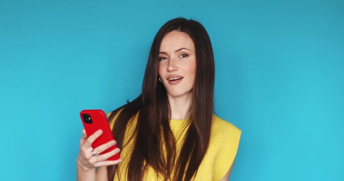Proud young woman looking at smartphone and point self arrogantly, feeling satisfied with success or praise, standing against blue background, expressing self-confidence and ego