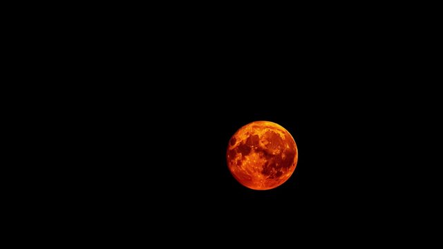 A large glowing orange moon sets in a black sky during a time lapse shot.