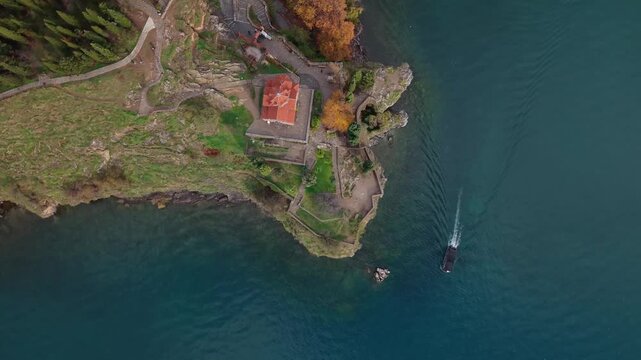 Top-down drone view of the cape with Saint John at Kaneo and a tourist boat along the shoreline of Lake Ohrid, showcasing the iconic church and scenic lakeside landscape