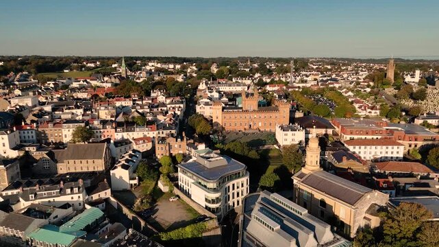 St Peter Port Guernsey slow low drone footage over Royal Court,St James and roof tops towards Elizabeth College with views across the skyline and whole Island on cloudless Summer day in bright sun