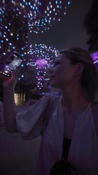 A tourist films a light show on her phone at Gardens by the Bay in Singapore City. Emotions from traveling, beauty, illumination, tree lighting, travel and tourism in Asia.