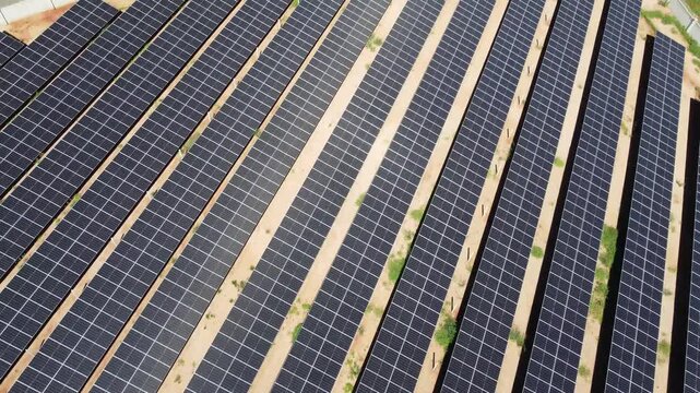 Aerial tilt-up shot starting from rows of photovoltaic solar panels to reveal a massive high-voltage transformer substation and electrical grid in Goiania, Brazil.