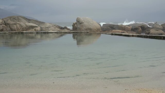 Tidal pool surrounded by huge beach boulders with crashing waves