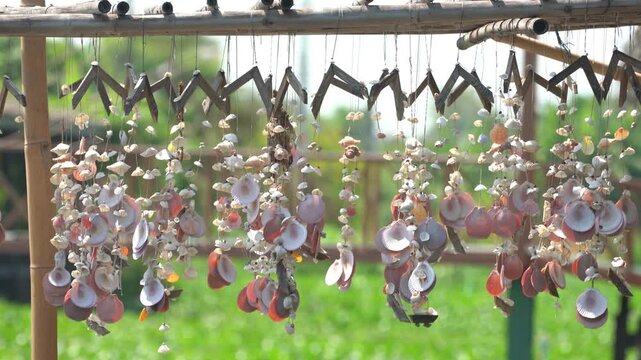 Sea shell mobile hanging and swaying in the gentle breeze with sunlight on green bokeh background in 4K seamless loop