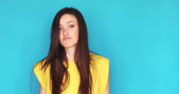 Confused and uncertain young woman shrugging shoulders and spreading hands in doubt isolated on blue background, hesitant female brunette looking at camera with I don't know expression, skeptical mood