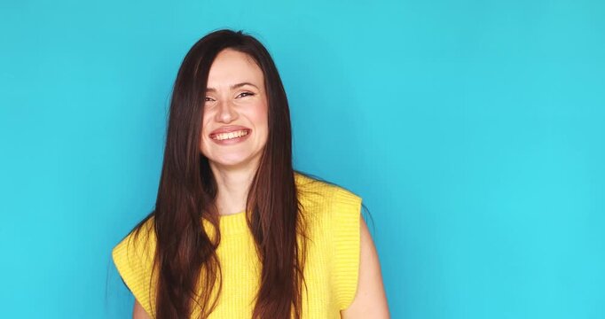 Extremely happy young woman showing double thumbs up and laughing loudly looking at camera isolated on blue background, excited female brunette celebrating success and great news, vivid emotions