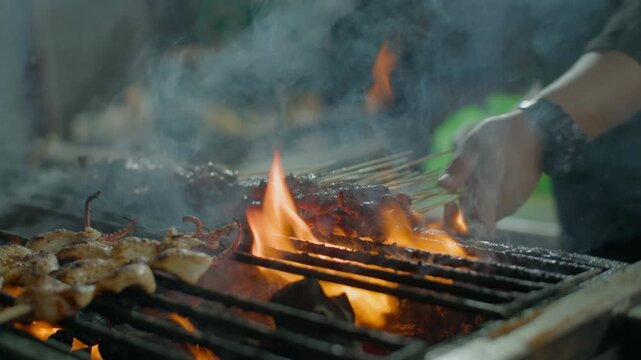 Chef grills Asian satay meat on barbecue grill. Beautiful skewers of grilled pork are turned over on fire, street food.