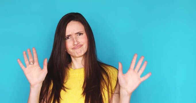 Young brunette woman in yellow top on turquoise background pointing finger asking is it you then strictly saying no with hand gesture of refusal, expressing disgust, dislike and strong rejection.