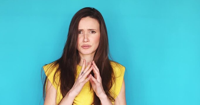 Young brunette woman in yellow top on turquoise background looking aside with worried and anxious face, gesturing with hands, showing skepticism, fear and disbelief, needing help and reassurance.