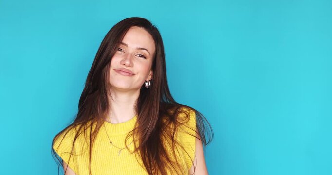 Playful young woman winking at camera with a cheeky face expression, showing tongue and smiling confidently, standing isolated on blue background. Portrait of beautiful girl flirting and having fun