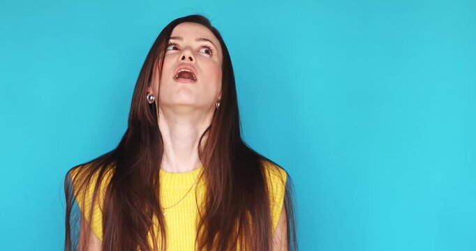 Portrait of Young Annoyed Brunette Woman in Yellow Vest Gesturing Blah Blah Blah with Hands and Rolling Eyes Feeling Bored and Skeptical Standing Against Bright Blue Background Looking Disinterested