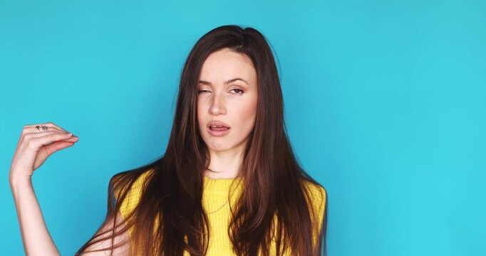 Portrait of Young Annoyed Brunette Woman in Yellow Vest Making Blah Blah Hand Gesture and Rolling Eyes Expressing Boredom and Skepticism Standing Against Bright Blue Background for Stock Footage Video