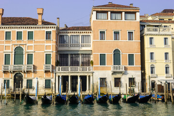 Fototapeta premium A row of gondolas are moored in a canal in front of historic buildings in Venice, Italy.