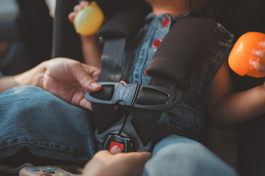 Close up of a mother's hands securely fastening a safety harness on a toddler in a car seat. Concept of child protection, parental care, and road safety during a family trip. Highlighting the importan
