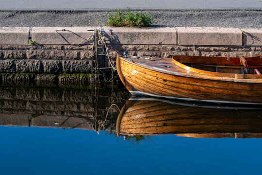 Classic wooden boat at harbor dock with strong reflection on water in Oslo Norway lit by sunlight along the waterfront quay